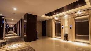 A modern hotel corridor with a reflective floor, elevators, and a patterned carpet.