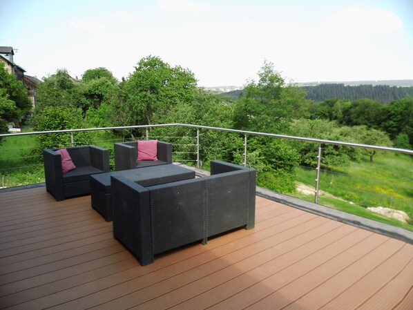 A deck with outdoor furniture and a view of a forested landscape.