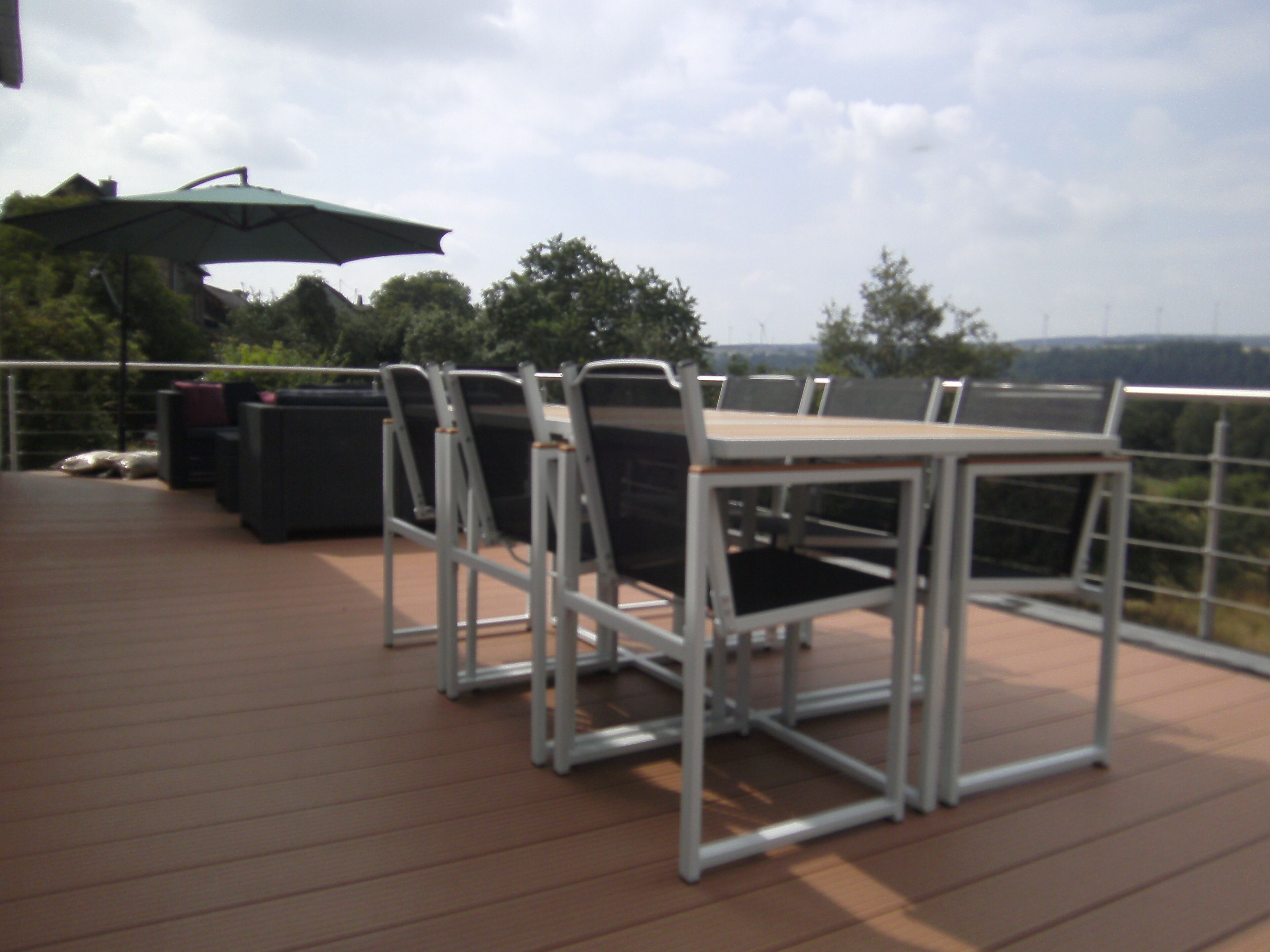 A deck with a table and chairs, an umbrella, and trash bins.