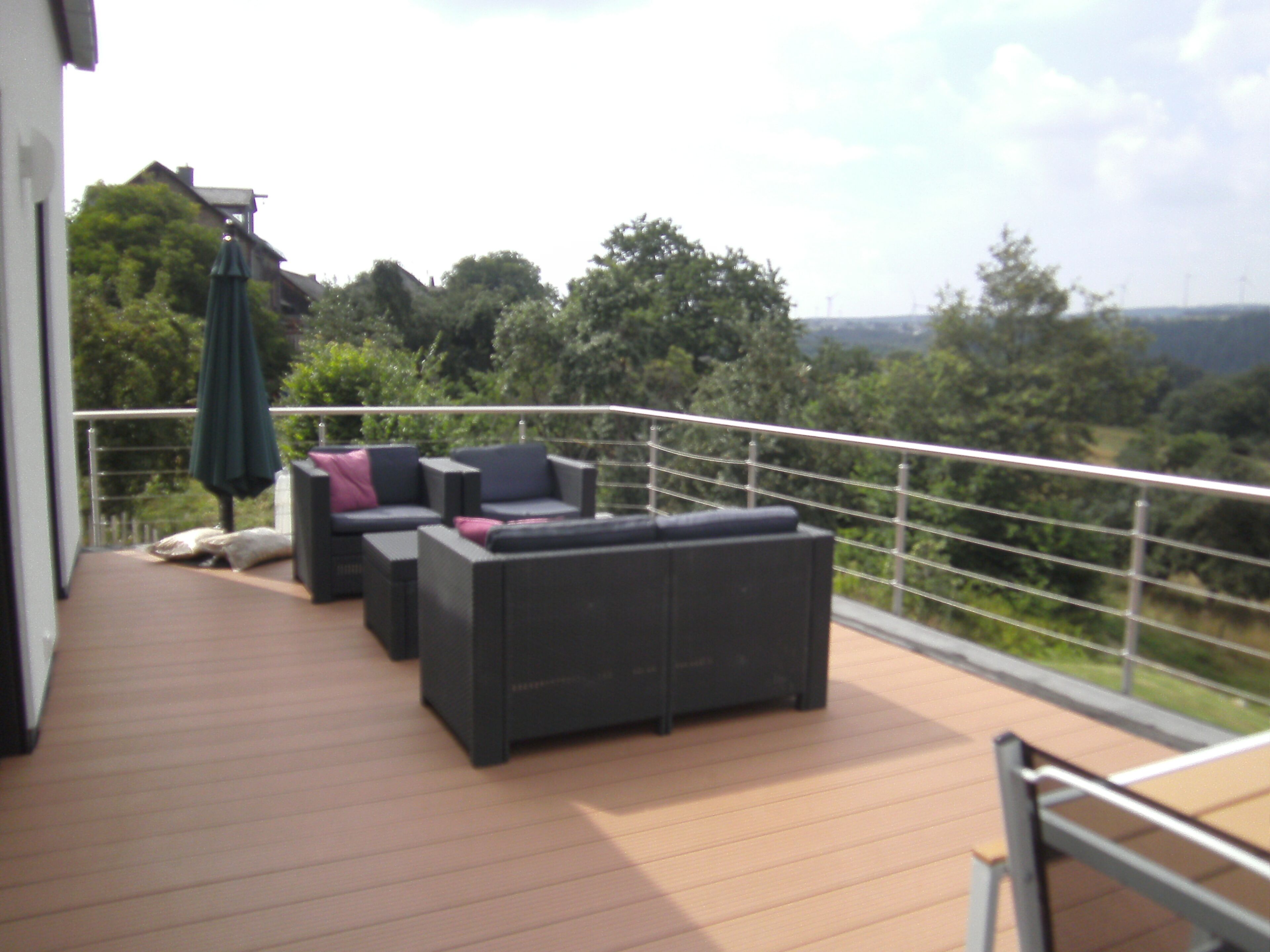 Un balcon avec un espace salon extérieur, une table et une vue sur la verdure environnante.