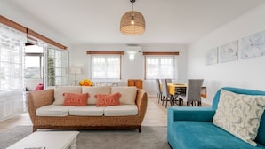 A living room with a wicker sofa, a blue sofa, a dining area, and a large window. - Casa da Adega - Holiday Home 2 Minutes from the Beach (Ribeira Chã)
