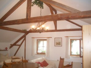 A room with a wooden ceiling, a chandelier, a bed, a table, and two windows with curtains.