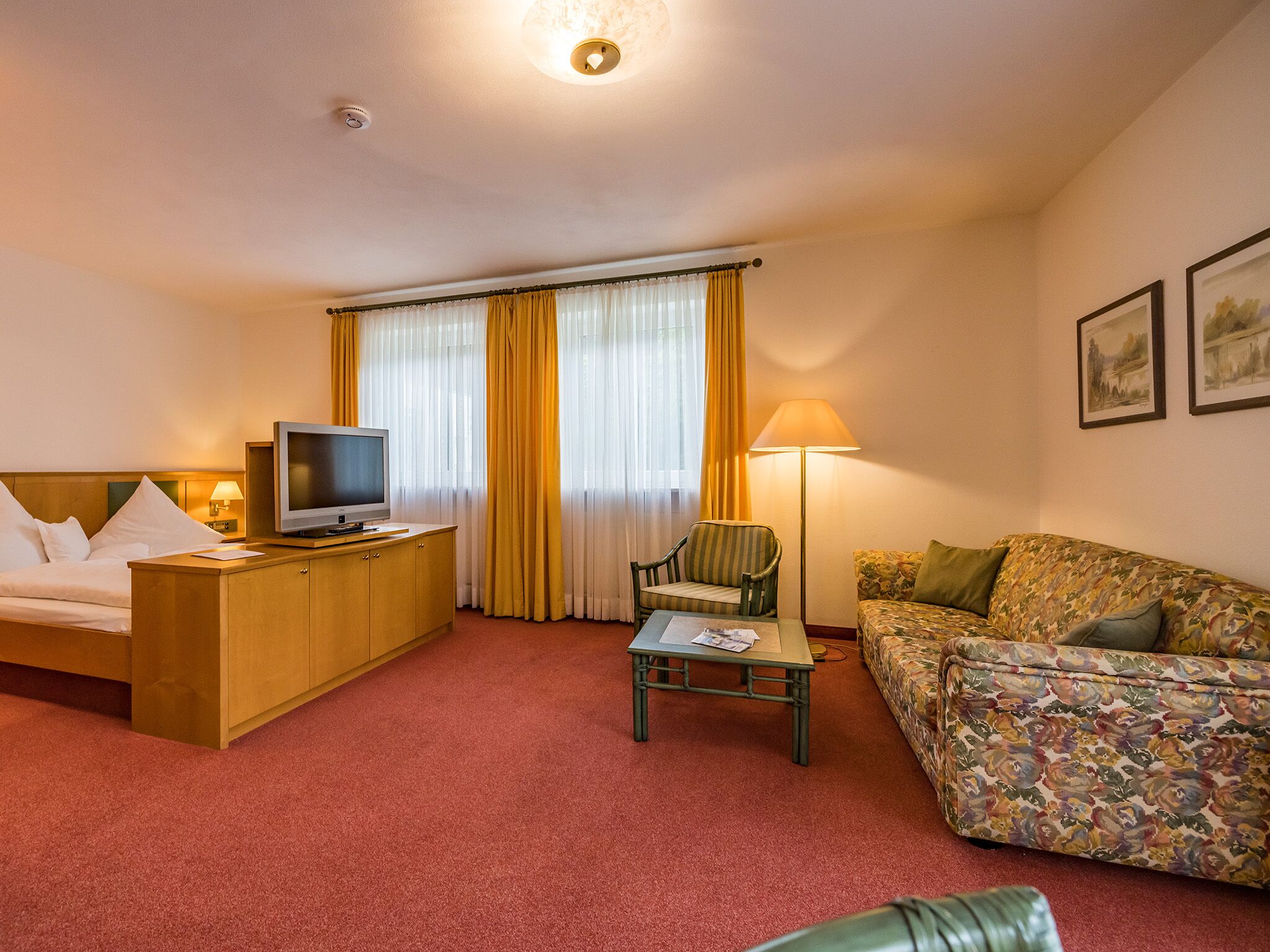 A hotel room with a bed, a TV, a desk, a chair, a sofa, and a lamp.