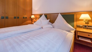 A hotel room with a double bed, two bedside tables, a nightstand, a wooden wardrobe, and a wall-mounted lamp. - Apartment 5, 6, 9, - 2 persons with balcony or terrace, 39sqm (Bad Reichenhall)