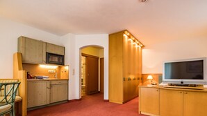 A compact hotel room with a kitchenette, a television, and a bathroom visible through an archway. - Apartment 5, 6, 9, - 2 persons with balcony or terrace, 39sqm (Bad Reichenhall)