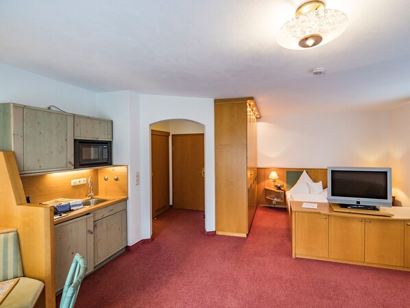 A compact hotel room with a kitchenette, a television, and a small desk.
