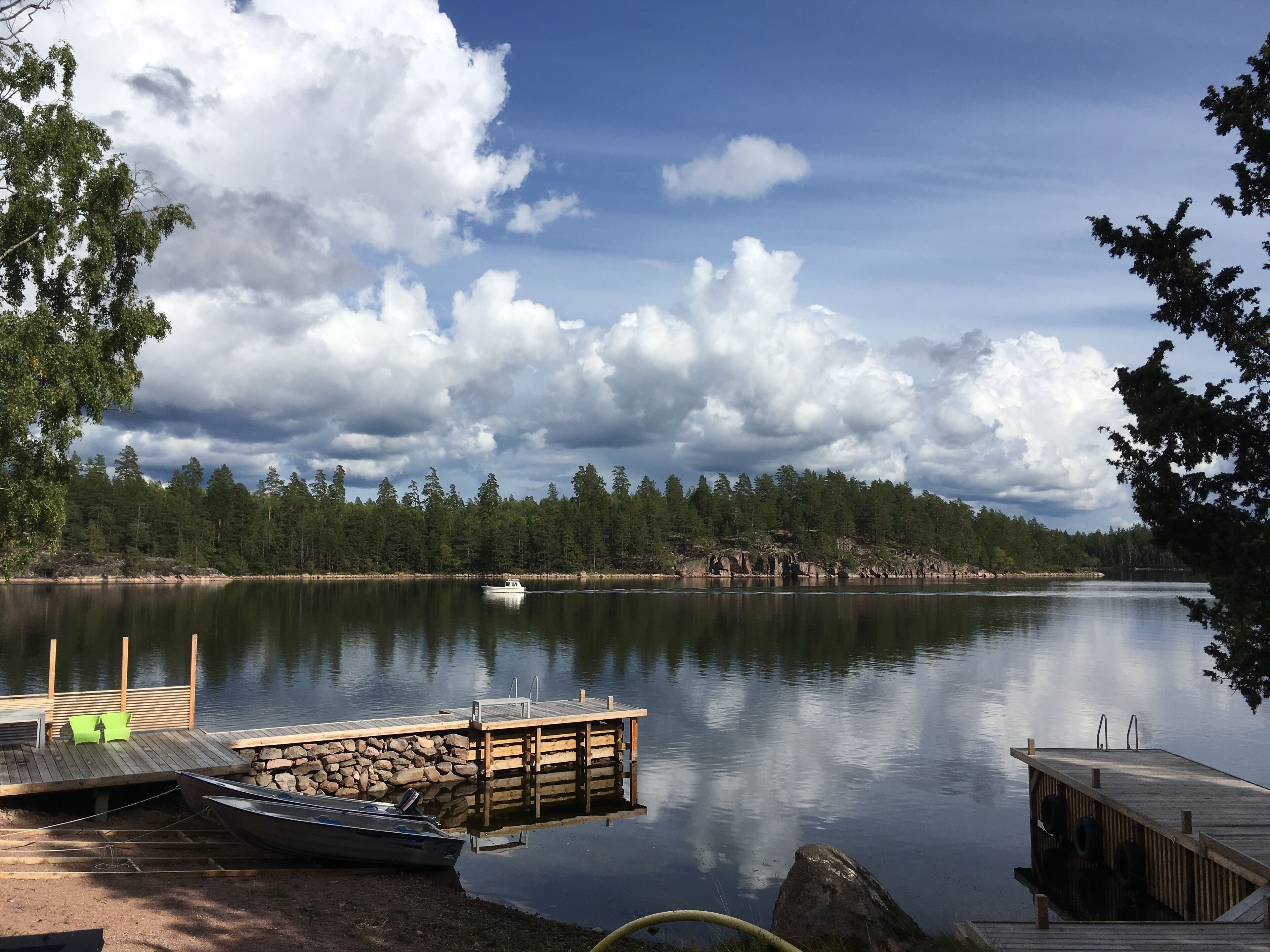 Un lac paisible, avec un quai et un bateau, entouré d’arbres et surplombé d’un ciel nuageux.