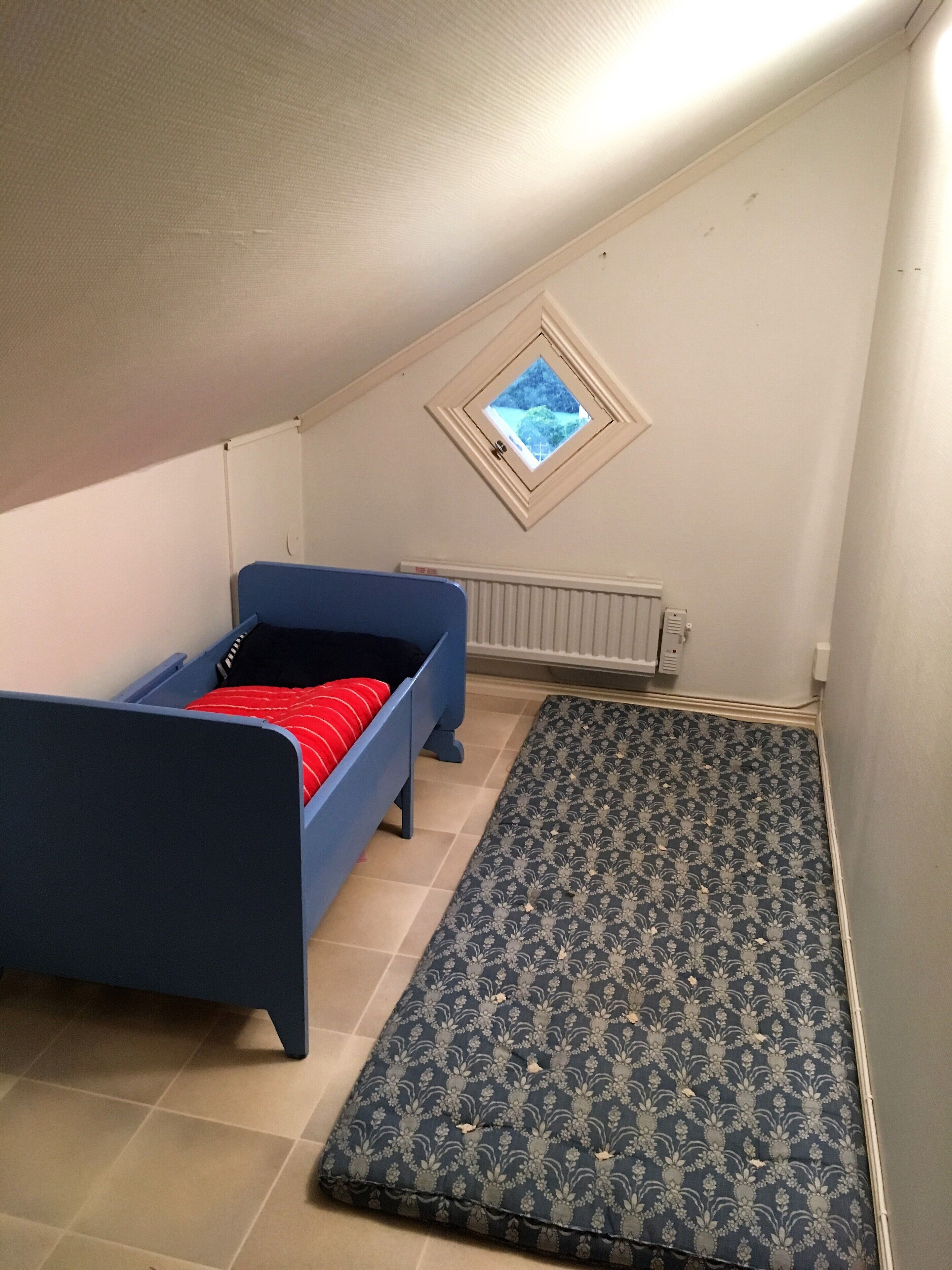 Ein kleines Zimmer mit einem Einzelbett, blauem Bettzeug, einem gemusterten Teppich und einem Dachfenster.