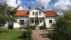 A two-story house with a white exterior, a red-tiled roof, and a balcony. - Large house with space for two families in a stunning farmhouse  (Tranås)