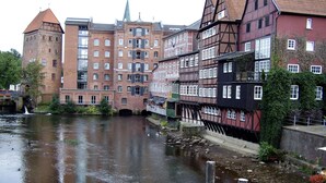 A historic European town with a river, traditional half-timbered houses, and a prominent tower. - Exclusive maisonette 83sqm, quiet, central location, in the old town (Lüneburg)