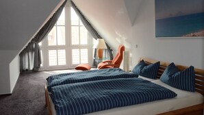 A bedroom with a sloped ceiling, a bed with striped bedding, a chair, a lamp, and a painting on the wall. - Exclusive maisonette 83sqm, quiet, central location, in the old town (Lüneburg)