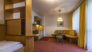 A compact hotel room with a kitchenette, a bed, a desk with a chair, and a window with curtains.