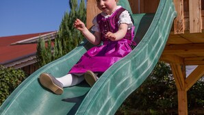 Un niño en un tobogán verde en una estructura de juego de madera.