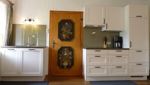 A kitchen with white cabinets, a wooden door with floral artwork, a coffee maker, and a knife block on the counter. - F Apartment Längauer Alm 52sqm, balcony, kitchen, 2 bedrooms and 1 bed-sitting room. (Ruhpolding)