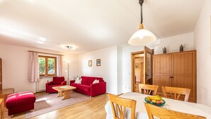 Ein gemütliches Wohnzimmer mit einem roten Sofa, einem Holzesstisch und einem durchgehenden Gang sichtbaren Küchenbereich.