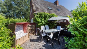 En uteplats med ett bord och stolar, en vadderad bänk och en pergola.