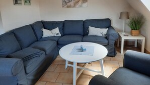 Ett modernt vardagsrum med en grå hörnsoffa, ett litet vitt bord och en lampa. Det finns två tavlor som hänger på väggen och en målning ovanför soffan.