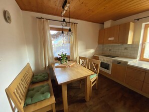 Una mesa de comedor de madera con sillas, un banco, una cocina con armarios de madera, una estufa y una ventana con cortinas.