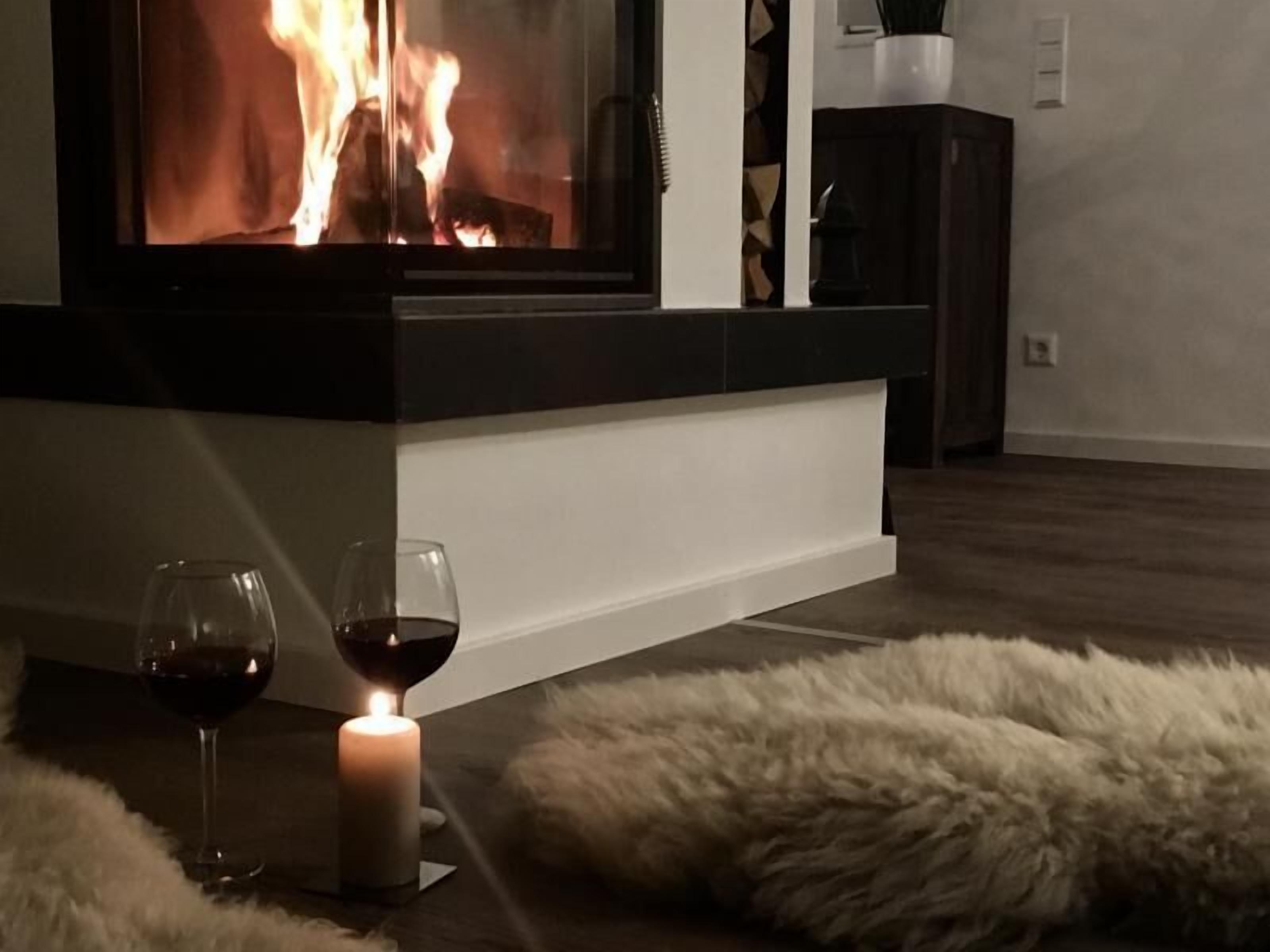 Ein gemütliches Zimmer mit Kamin, zwei Gläsern Rotwein und einem flauschigen Teppich.