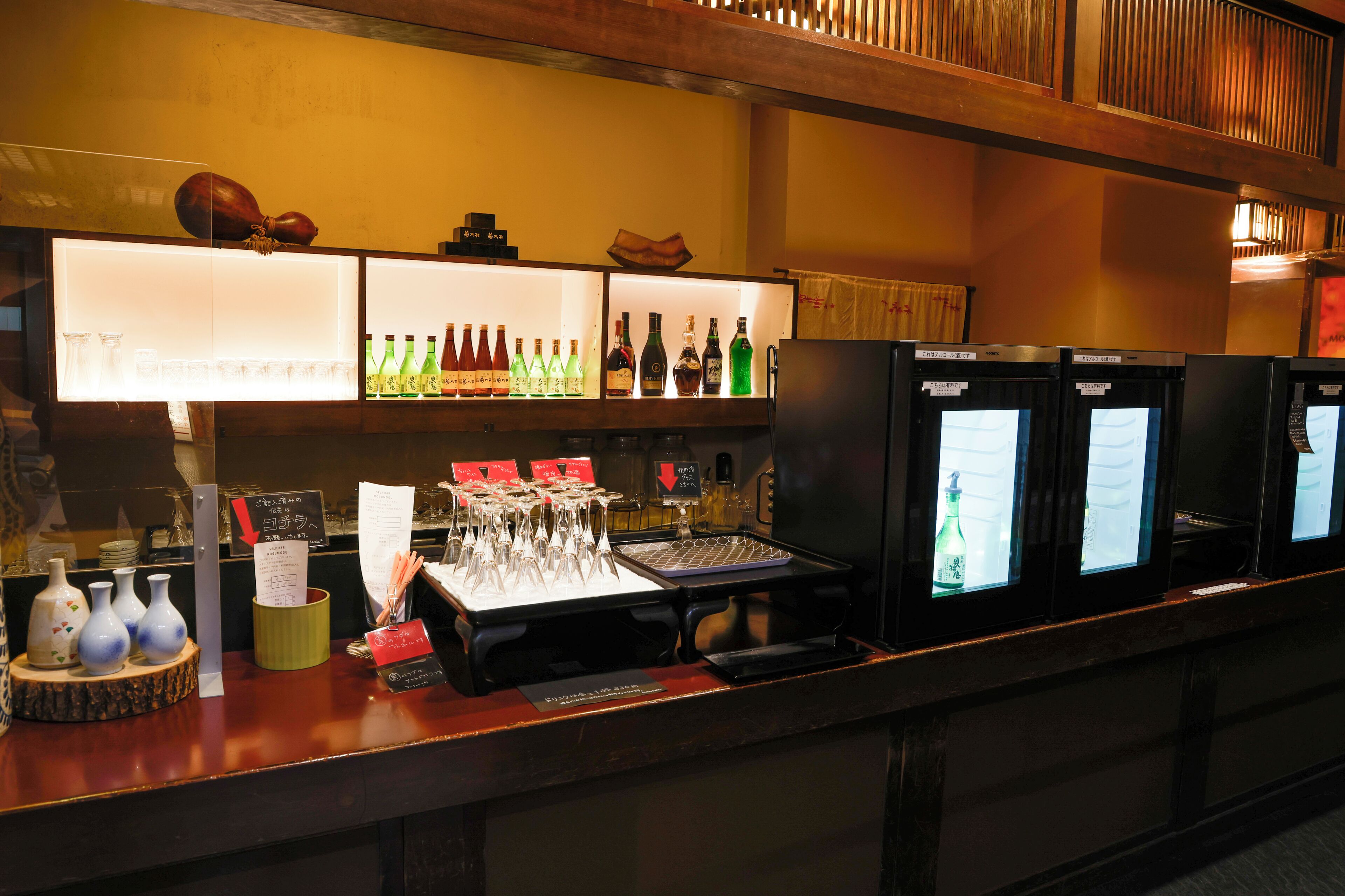 Angolo bar con scaffali pieni di bottiglie, bicchieri e una cassa.
