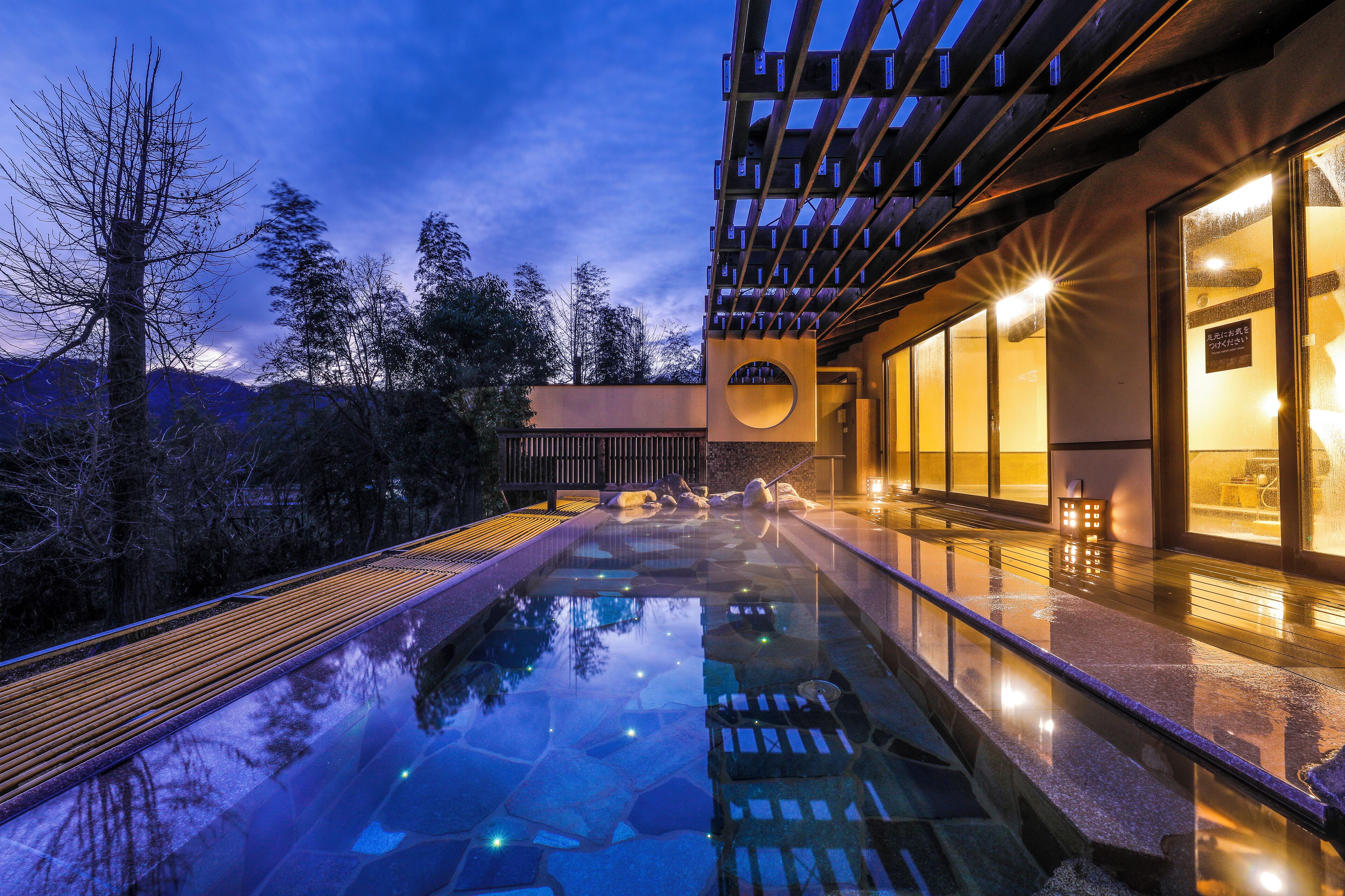 A modern building with a reflective pool, wooden deck, and a view of mountains.