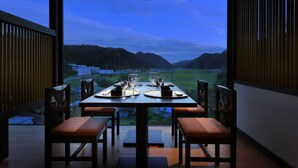 Un coin repas avec une table dressée pour deux personnes, offrant une vue panoramique sur les montagnes et une ville lointaine.