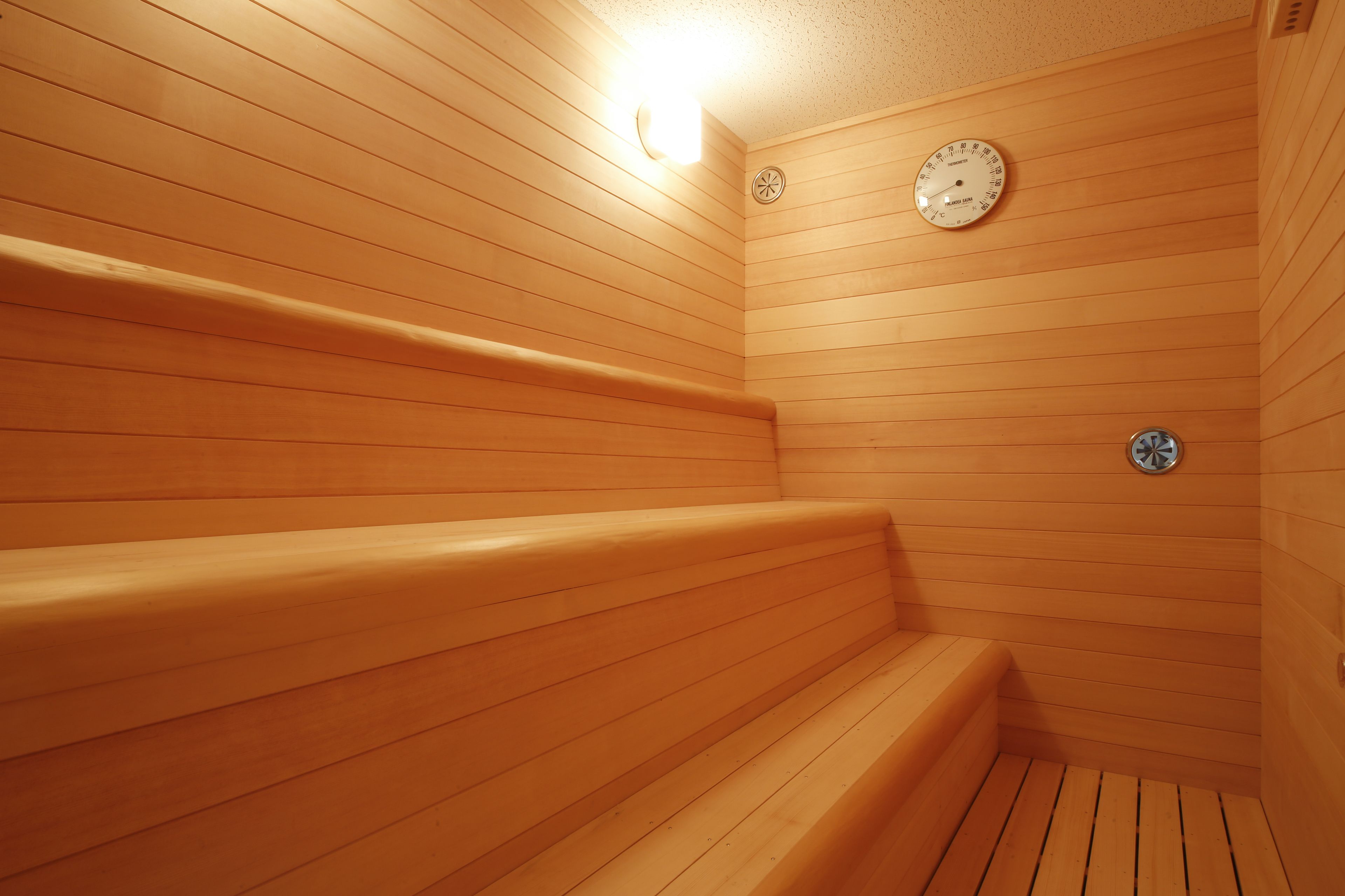 Una sauna de madera con bancos y un termómetro fijado a la pared.