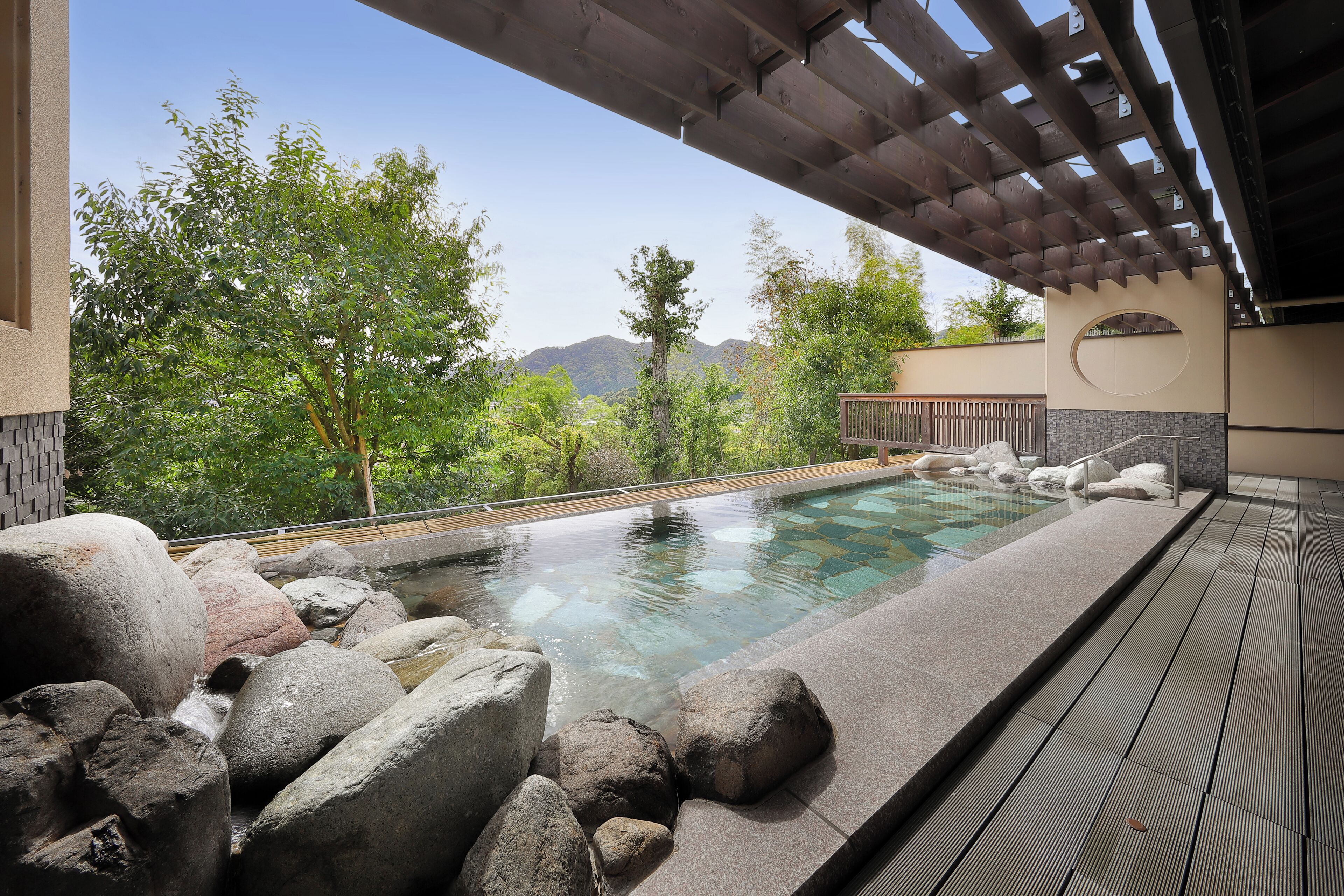 Zona de piscina con rocas grandes, una pérgola y vistas a las montañas.