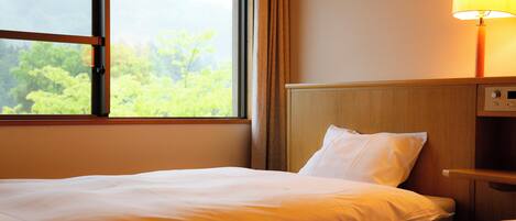 A hotel room with a bed, a nightstand, a lamp, and a window with a view of greenery.