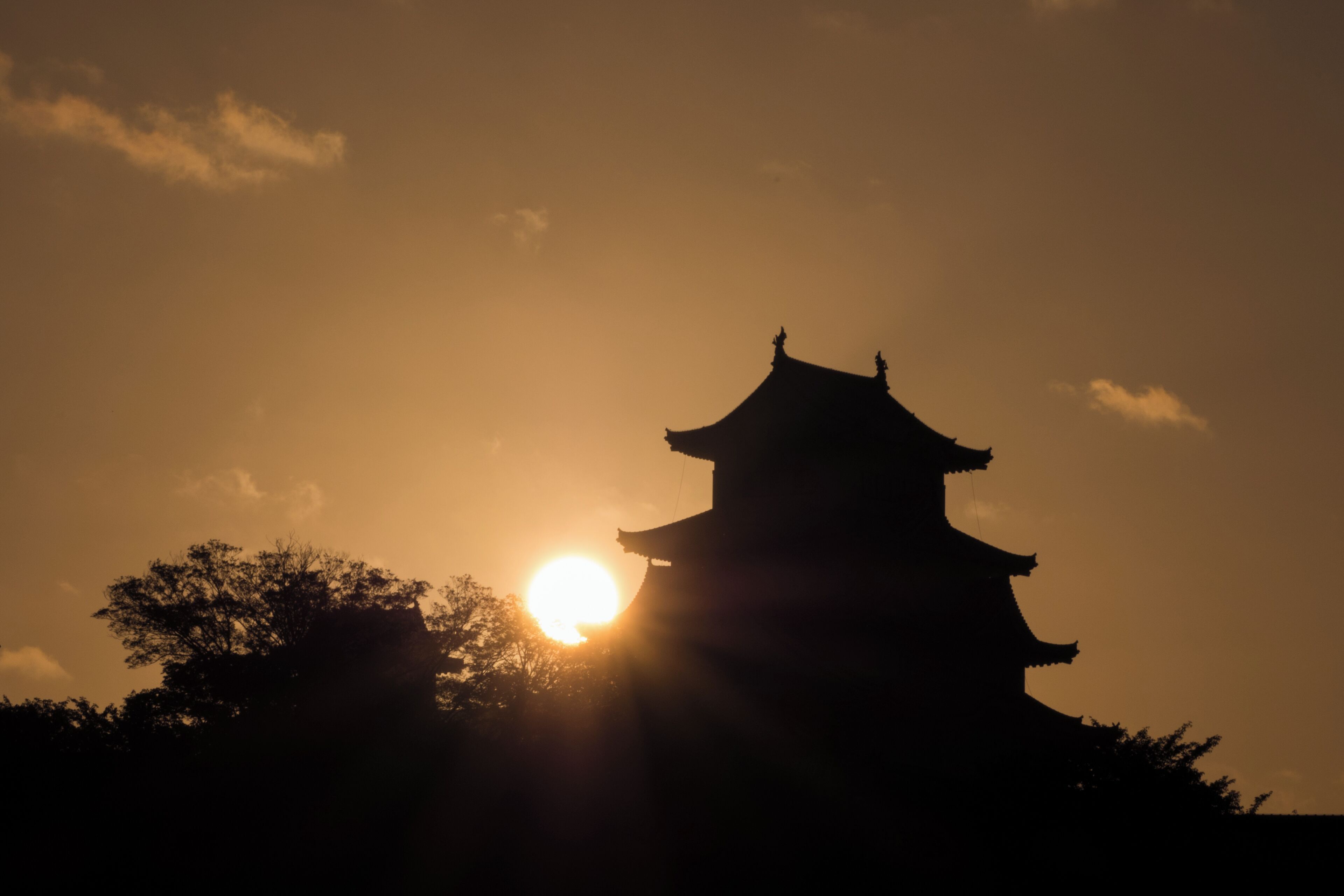 A silhouette of a traditional building against a sunset sky.