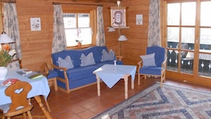 A cozy cabin interior with a blue sofa, a small table, and a chair. - Ferienhaus für 2 Personen (Berchtesgaden)