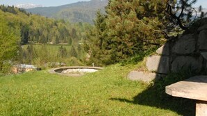 A grassy outdoor area with a stone bench, a stone wall, and a view of a forested valley with mountains in the background. - Ferienhaus für 2 Personen (Berchtesgaden)