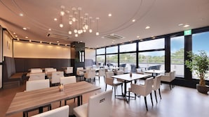 A modern dining area with tables and chairs, large windows, and a ceiling with hanging lights.