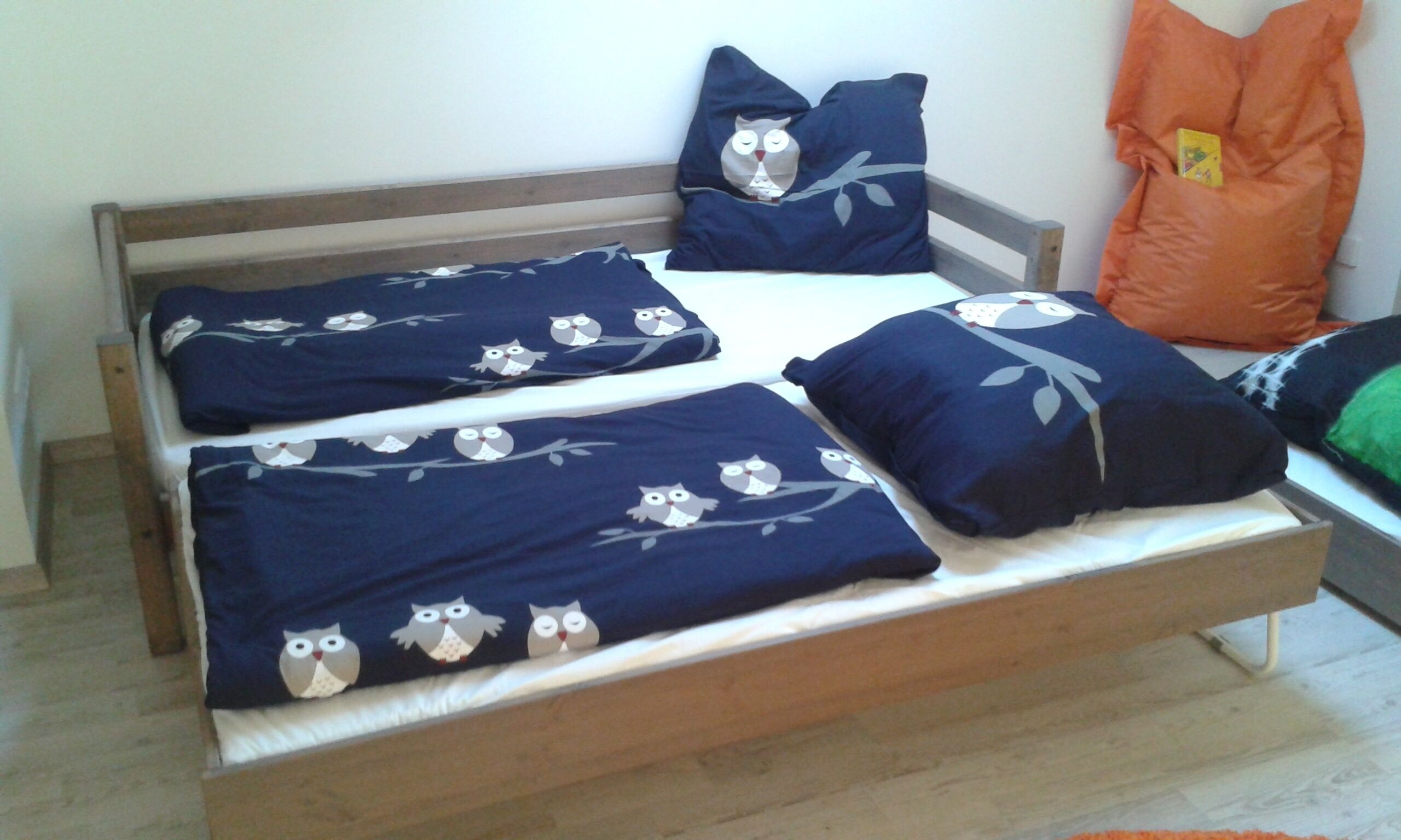 Ein Bett mit Holzrahmen, dunkelblaues Bettzeug mit Eulenmuster und passende Kissen.