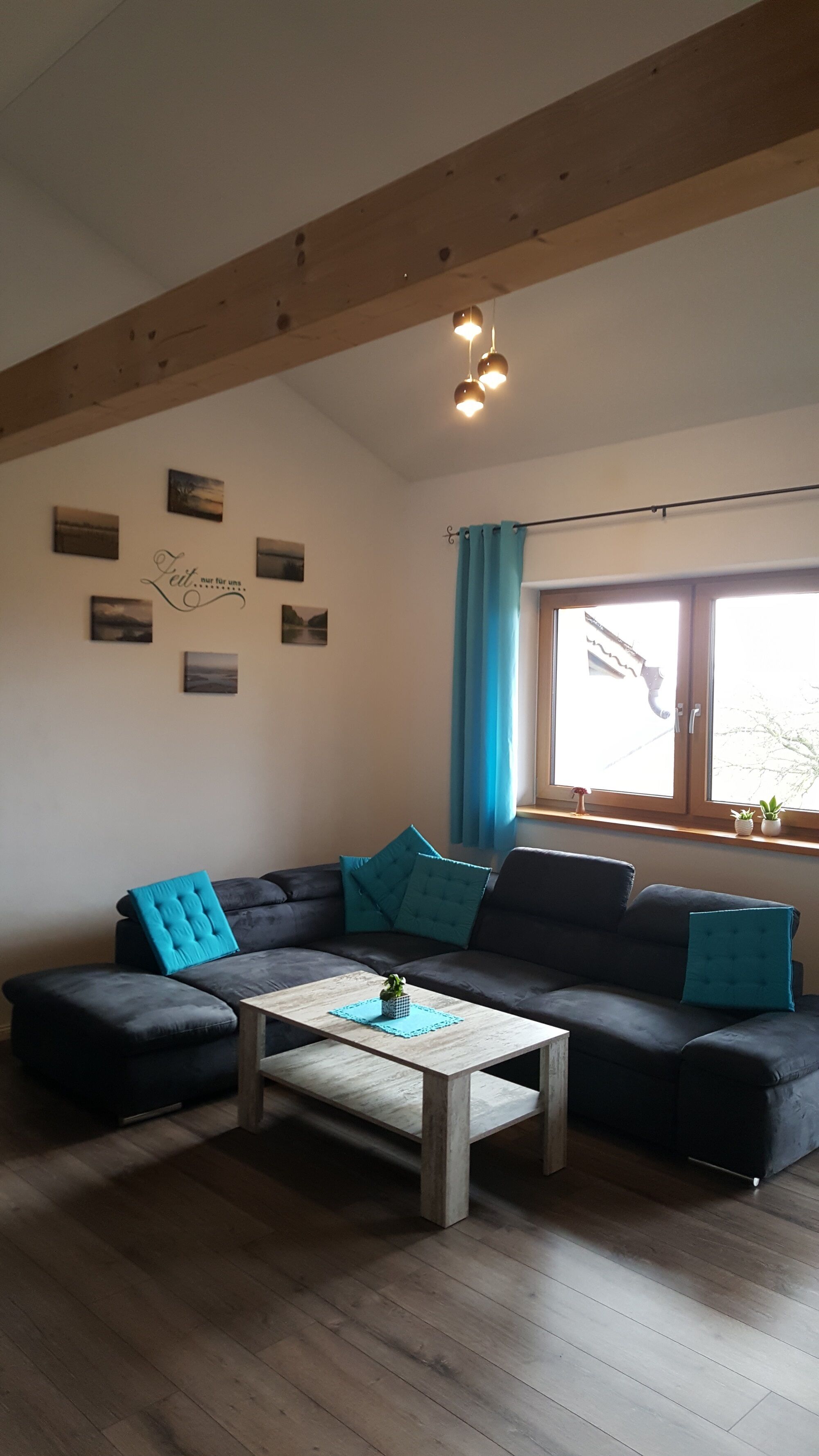 A living room with a dark-colored sofa, a light wooden coffee table, and a window with blue curtains.
