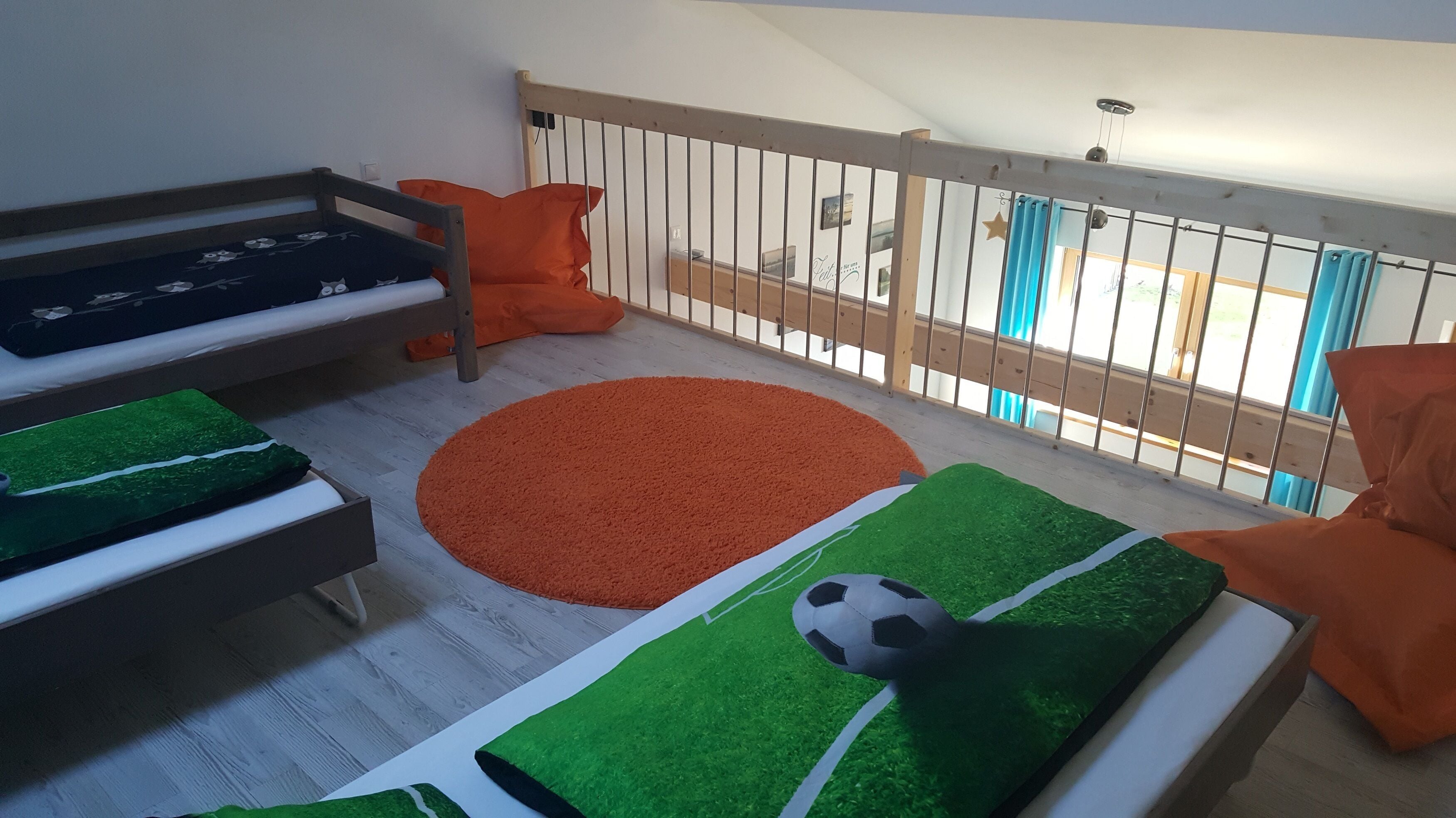 Un'area giochi per bambini con una cuccetta, un tappeto rotondo arancione e un pallone da calcio su un prato sintetico.