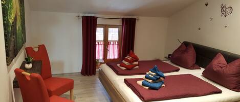 Habitación de hotel con una cama, dos sillas rojas, una mesita con una planta y un cuadro en la pared.