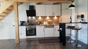 Una cocina moderna con gabinetes blancos, una estufa negra y una zona de bar con taburetes.