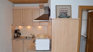 Une cuisine compacte avec des meubles en bois, un évier en acier inoxydable, une machine à café et un réfrigérateur blanc.