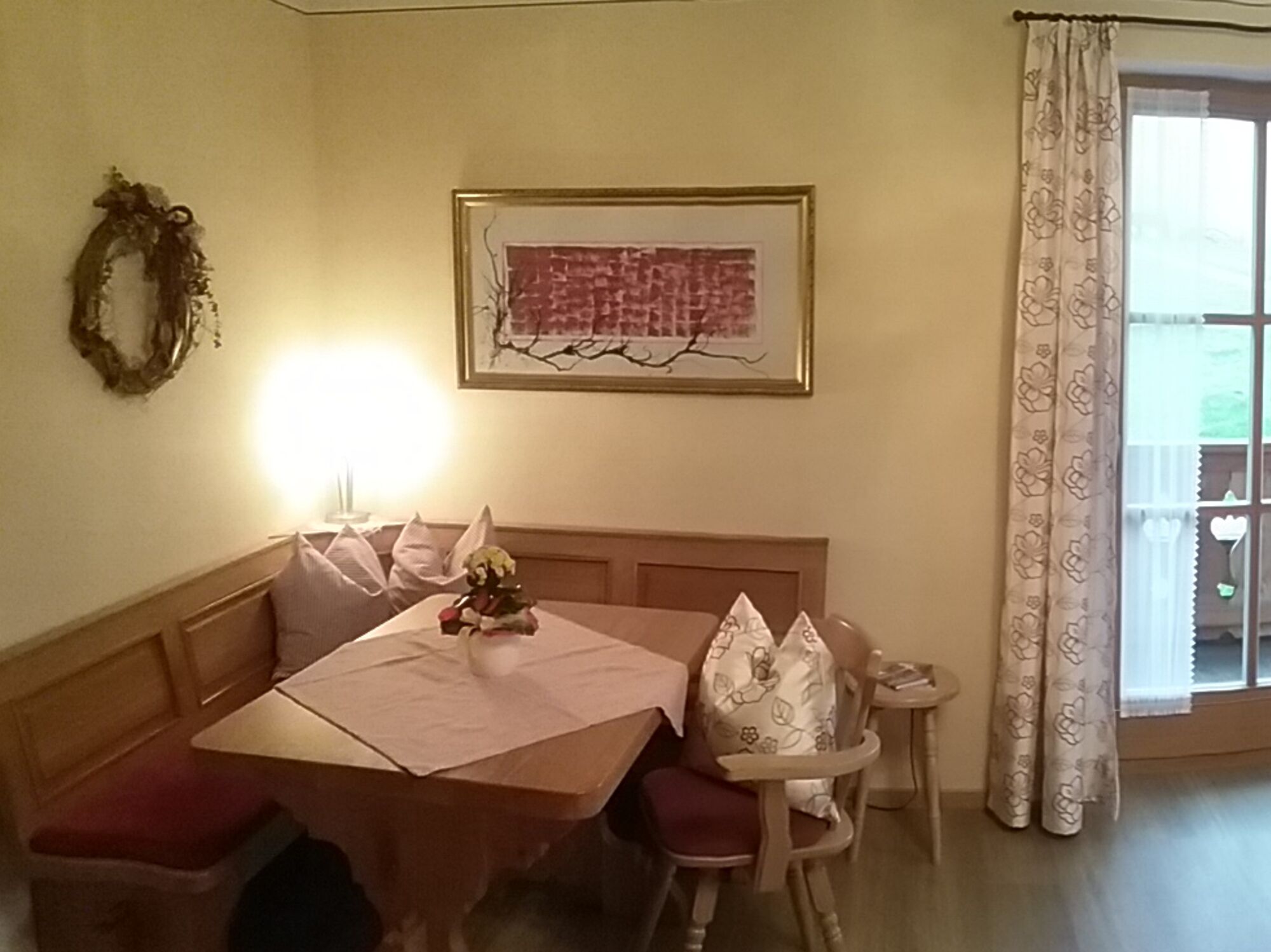 En matplats med ett träbord och stolar, ett litet sidobord, en dekorativ krans och ett inramat konstverk på väggen.