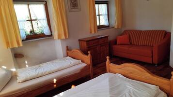 Ein Zimmer mit zwei Einzelbetten, einer Holzkommode, einem roten Sofa und zwei Fenstern mit gelben Vorhängen.