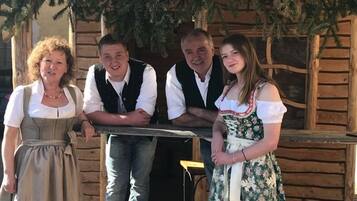 Eine Gruppe von Menschen steht auf einem hölzernen Deck, im Hintergrund ein rustikales Gebäude.