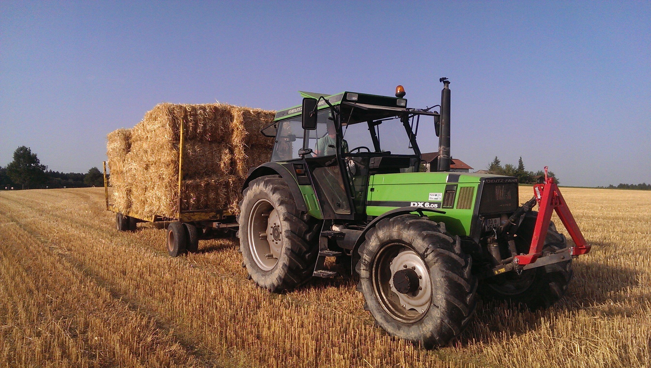 Een groene tractor met aanhanger, beladen met strobalen in een veld.