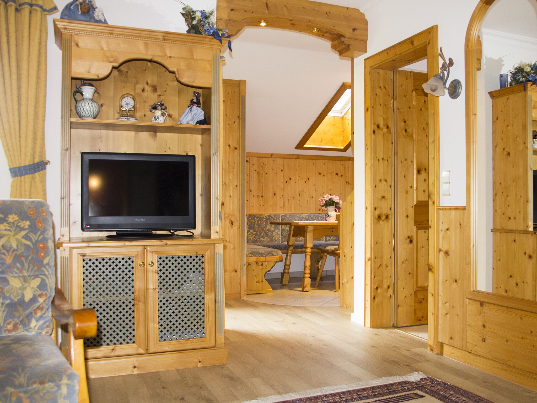 Ein Holzinterieur mit einem Fernseher auf einem Schrank, einem Sofa, einem Esstisch mit Stühlen und einer Holztür.