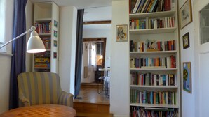 Una habitación con una mesa de madera, un sillón a rayas, una estantería y un escritorio con una lámpara.