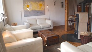 Una sala de estar con un sofá blanco, un cuadro de margaritas, una mesa de madera y una chimenea.