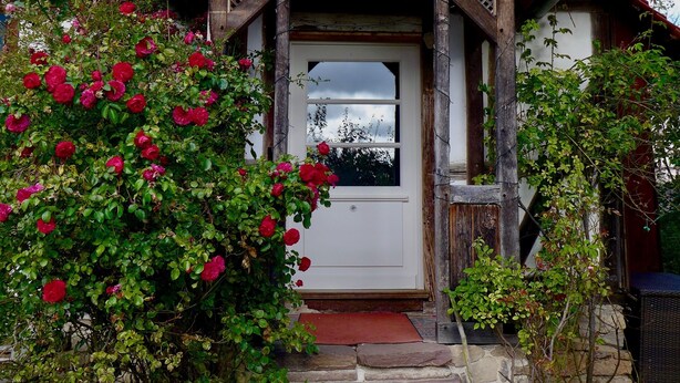 Una casa de madera con techo de tejas rojas, un porche de madera y una escalera de piedra que lleva a la puerta.