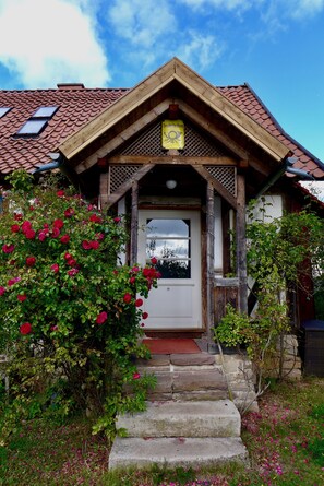 Una casa de madera con techo de tejas rojas, un porche de madera y una escalera de piedra que lleva a la puerta.