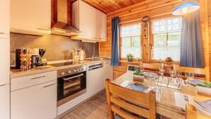 Une cuisine de style rustique, avec des murs en bois, comprenant une cuisinière, un four et un évier. Une table à manger est dressée avec des assiettes et des verres.