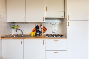 A kitchen with white cabinets, a stainless steel sink, a stove, and a tiled backsplash.